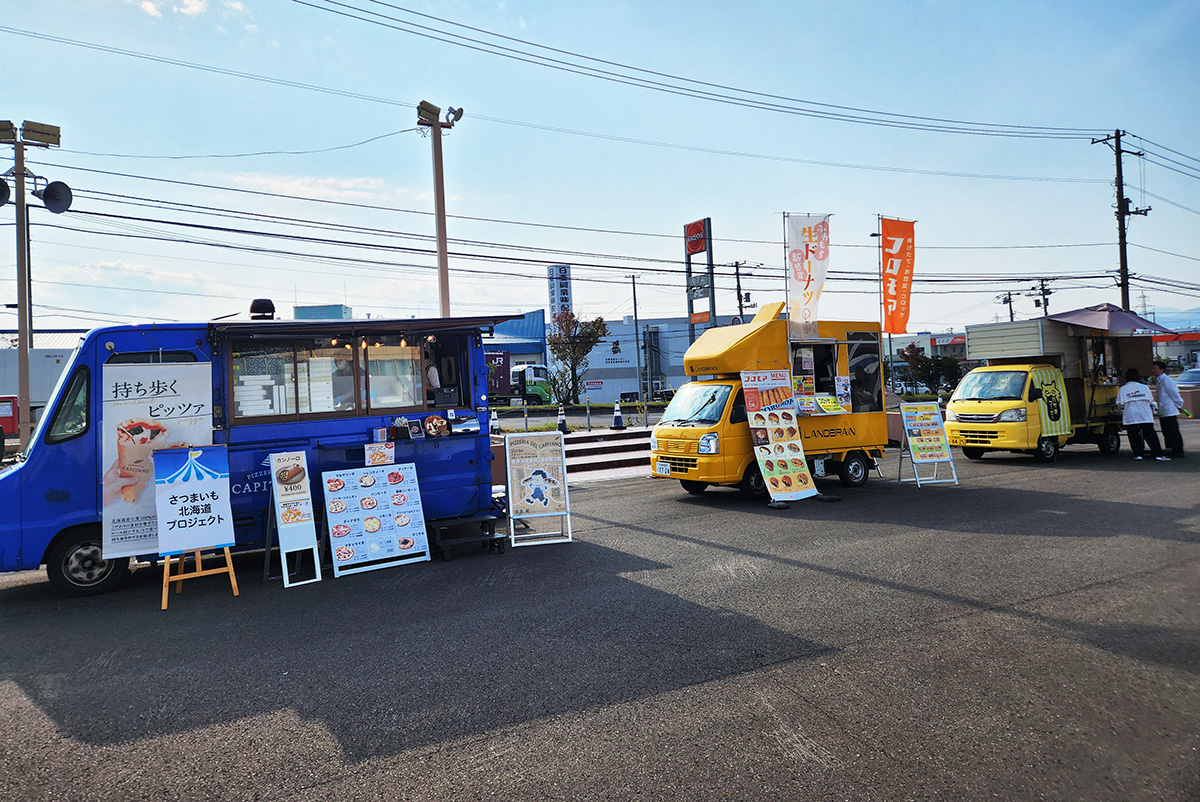 快晴の空の下、キッチンカーが3台並んでいる。左からPIZZERIA DEL CAPITANO（ピッツェリア　デル　カピターノ）、コロモア、バケネコーヒーのキッチンカーだ。